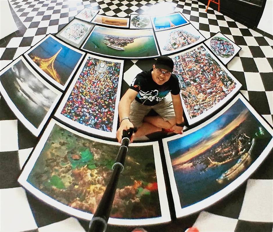 Loh taking a creative selfie while being surrounded by pictures of Penang for the exhibition.