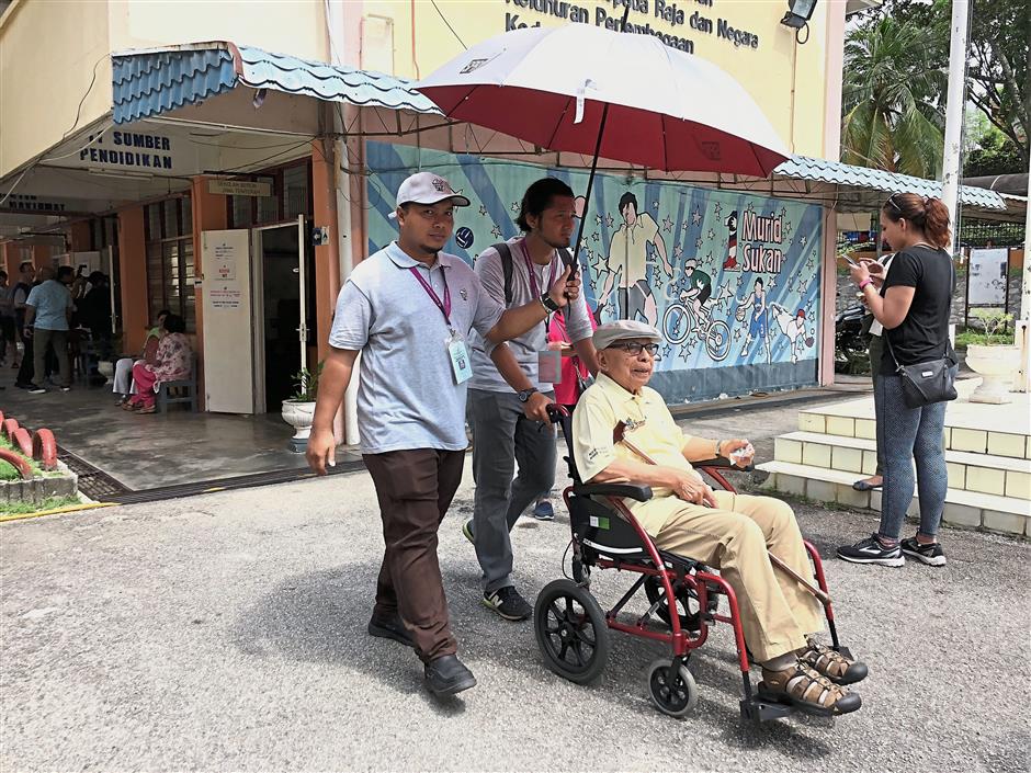 A wheelchair-bound senior citizen being escorted to his stream at SK Bukit Damansara.