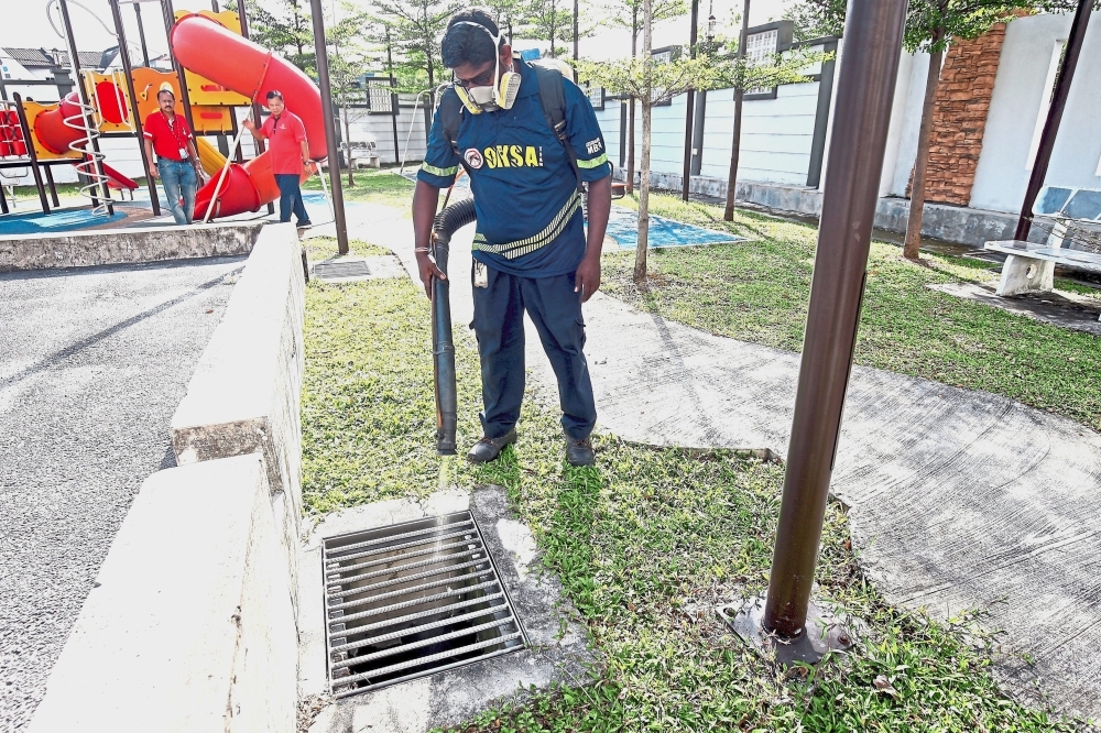 A field worker spraying a thin film of oil and chemical into the drains filled with stagnant water within the compound of Damai Apartments. — Photos: FAIHAN GHANI/The Star