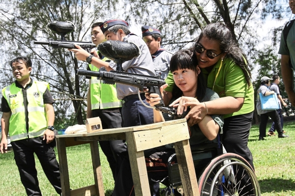 Wheelchair-bound Lim Chun Tian guided by a volunteer while playing paintball.