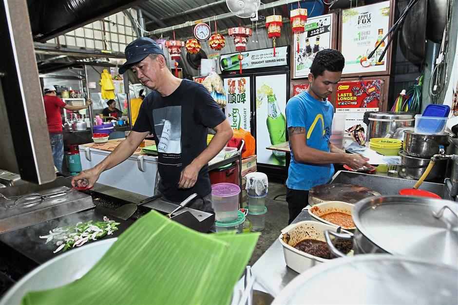 The cook, known as Ah Keong (left) preparing the grilled fish for customers.