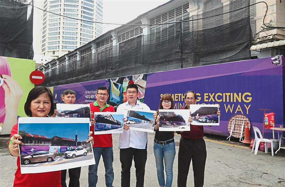 Under wraps: (Above) A purple hoarding covering a row of heritage buildings at the junction of Jalan Gurdwara-Lebuh Noordin. (Right pic, on the left) Ng and her team showing more photos of buildings covered with purple hoardings while standing in front of a sealed up property in Bertam Lane. — ZHAFARAN NASIB/The Star