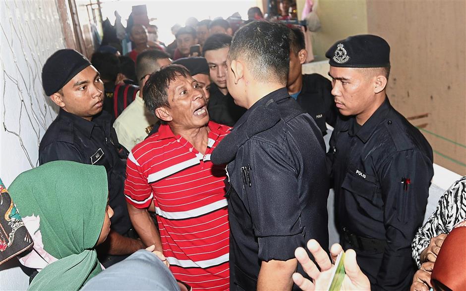 Why me?: Police officers arresting Kutnan after he refused to vacate his home. (Below) Other residents, some with children, were also told to vacate the premises. ?— ZHAFARAN NASIB/The Star