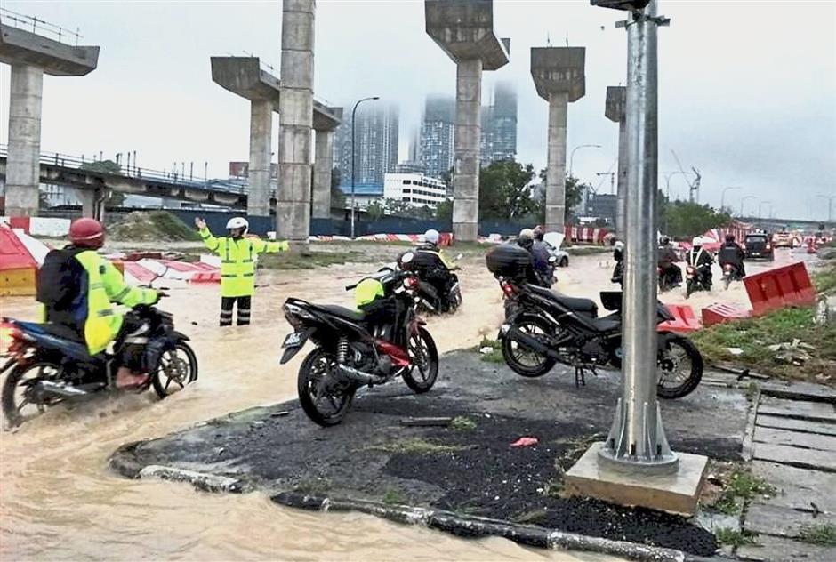 (Left) Traffic police personnel were deployed to manage traffic flow as well as to close some roads.(Below) Motorists inching their way through the flood waters in Klang.