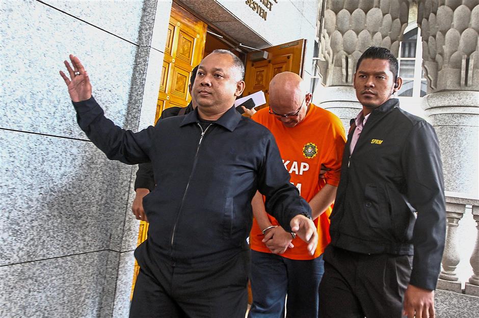 Taken away: Officers escorting one of the men out of the courthouse in Putrajaya.