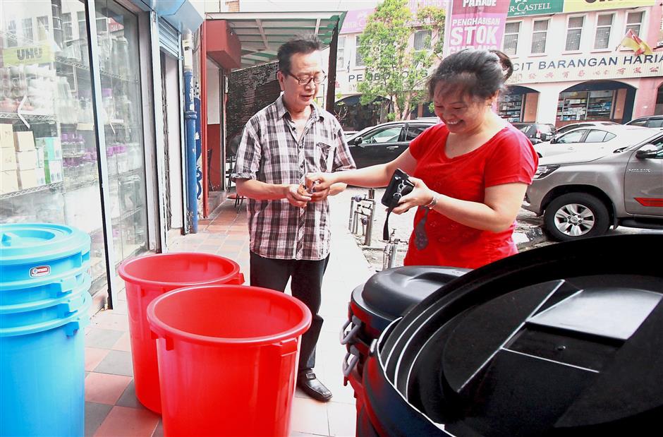 Chow Hung Khin busy attending to a customer who purchased two plastic containers from his shop in Jalan Gopeng, Klang.