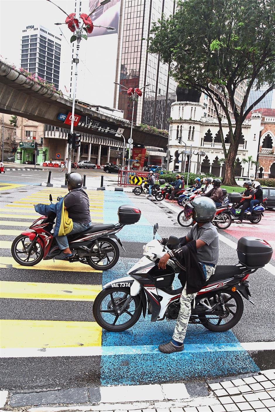 Motorcyclists stopping at a traffic light intersection on the blue lane meant for cyclists.
