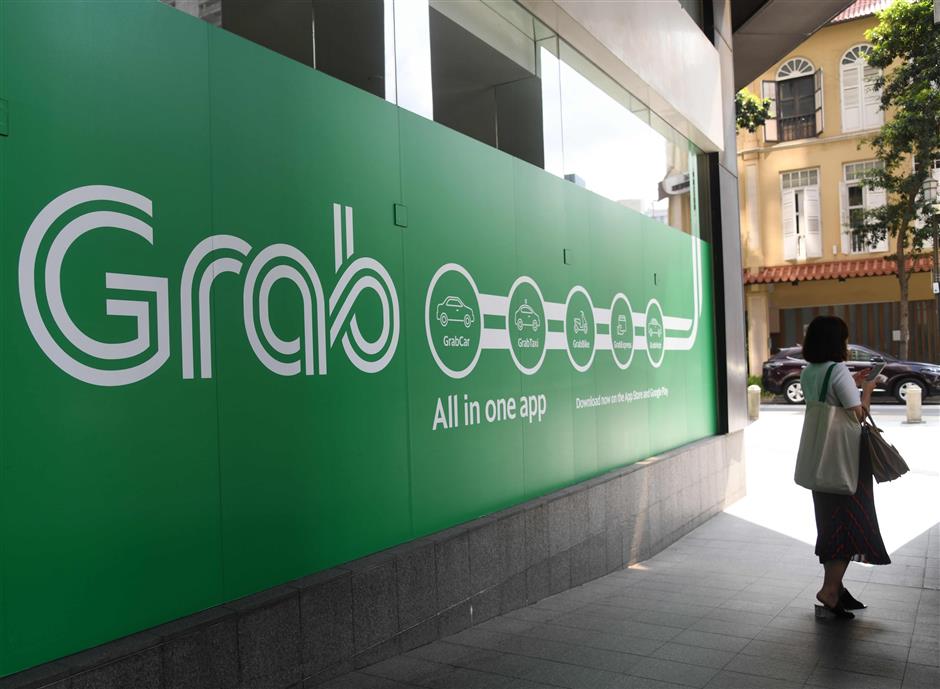 A woman stands outside the Grab transport office in Singapore on June 13, 2018. Toyota said on June 13, that it was investing 1 billion US dollars in Asia ride-share company Grab, as the Japanese automaker looks to expand beyond its core business into the 'mobility' sector. / AFP PHOTO / ROSLAN RAHMAN