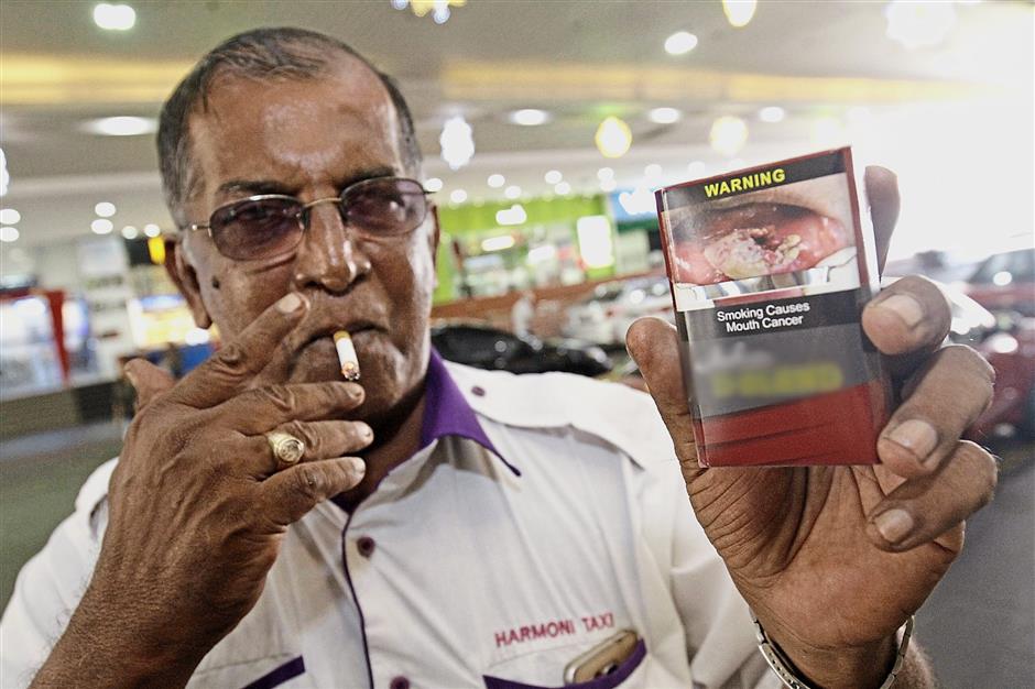 Mohd Kamaruddin showing the health warning on a cigarette packet. He is eager to quit smoking but says it’s a slow process.