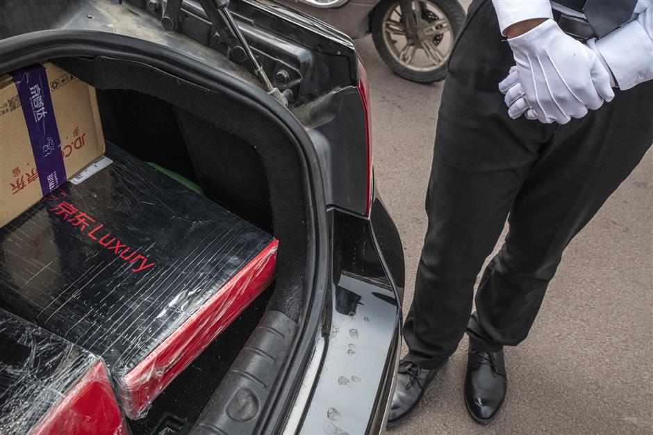A driver for JD.com Inc.'s Luxury Express delivery service stands next to the trunk of his car containing customers' parcels in Beijing, China, on Thursday, May 16, 2019. Big names in luxury are teaming up with internet companies to offer sales and services like JD's white-gloved butler-style delivery that are rare in the U.S. Photographer: Gilles Sabrie/Bloomberg