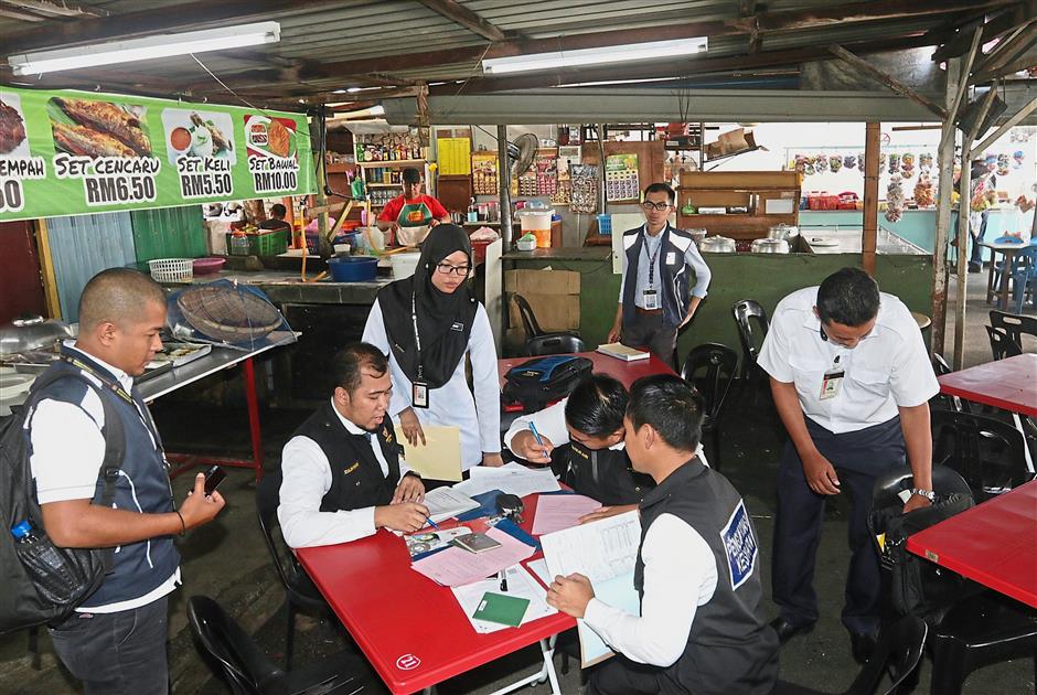 State Health Department enforcement officers writing out summons notices during the ‘Penang Sihat’ operation at a food stall in Bayan Lepas, Penang. — Photos: ZHAFARAN NASIB/The Star
