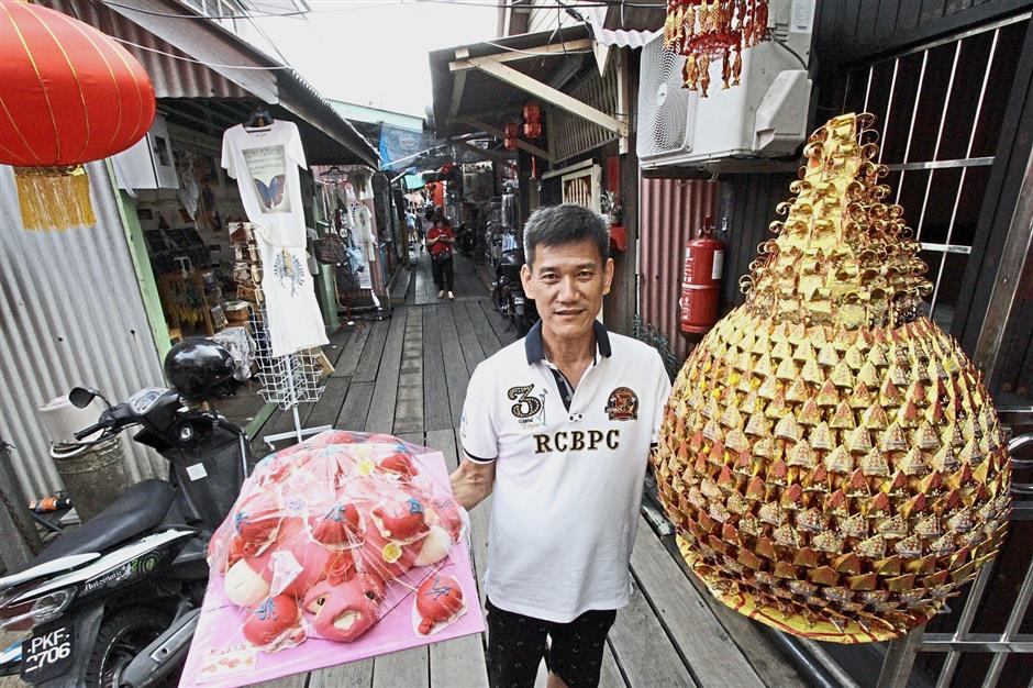 A resident showing a giant pineapple-shaped thnee kong poh and mee koo (tortoise buns) for the Jade Emperor’s birthday celebration at Chew Jetty, George Town. Lim (right pic, seated) and Lee preparing offerings for the celebration. — Photos: CHAN BOON KAI/The Star