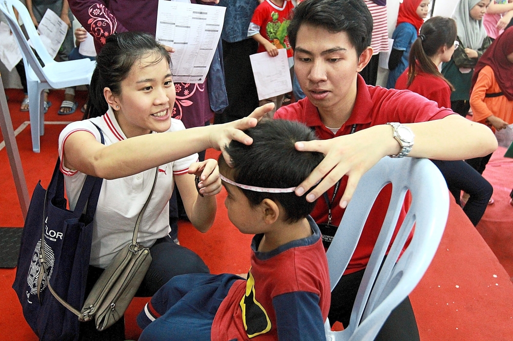 Dr Heng Kai Voon (left) and medical undergraduate Danial Haziq taking the measurements of a child in PPR Lembah Subang.
