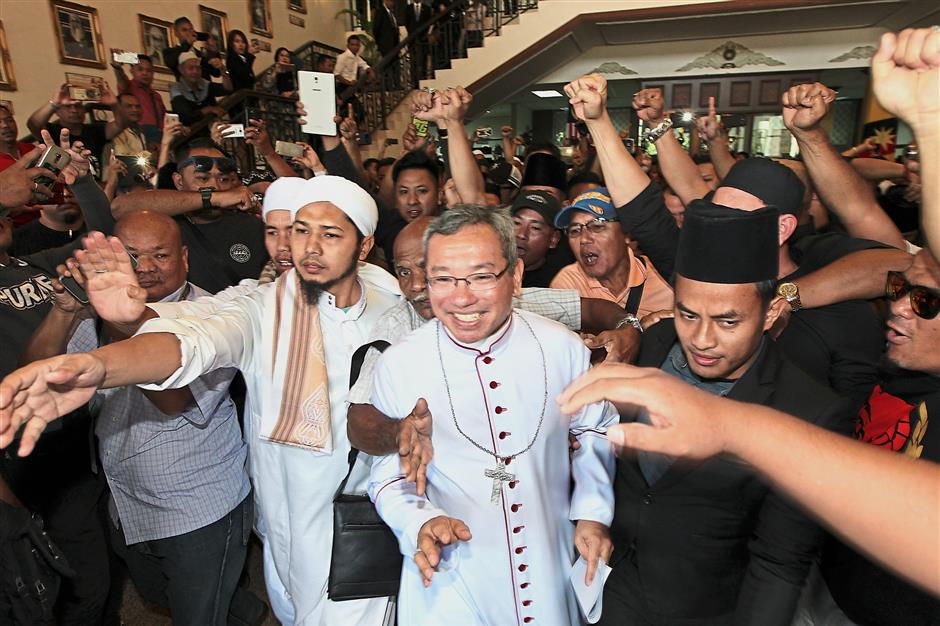 We’re here for you: Poh (centre) being protected by a group of Muslims as he leaves the Kuching court complex.