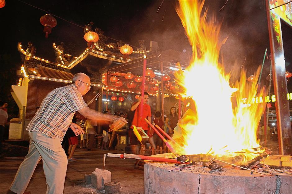 An elderly devotee burning prayer paraphernalia at the temple compound.