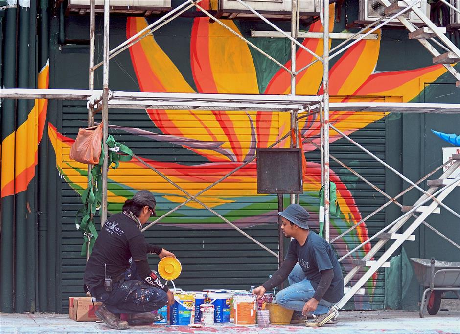 Street artists meticulously painting a giant heliconia on a building.