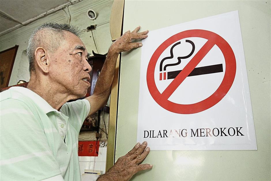 Teoh putting up a no-smoking sign at his coffee shop. He says his customers have expressed displeasure over the ban.