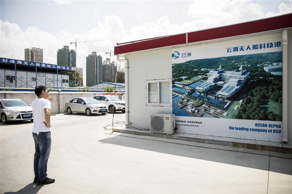 A man stands in front of a banner featuring an illustration of the new Oceanalpha Co. headquarters in Zhuhai, China, on Thursday, May 18, 2018. Oceanalpha, one of a handful of companies around the globe specializing in ocean-going drones that operate on the surface, has fired the interest of some of China's biggest venture capitalists. Photographer: Qilai Shen/Bloomberg