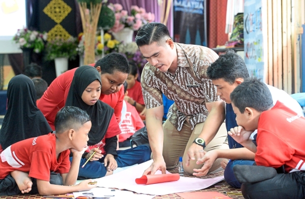 Cikgu AG (in brown batik) guiding his pupils to make Teachers’ Day cards to present to their teachers.