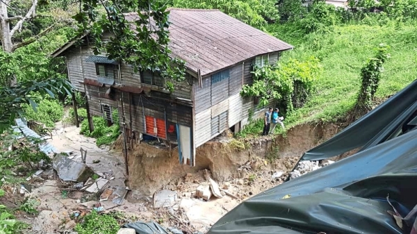 Dangert zone: A JKR personel inspecting the cave-in in Jalan Lembah Permai and (inset) the abandon squarter house. — ZAINUDIN AHAD/The Star