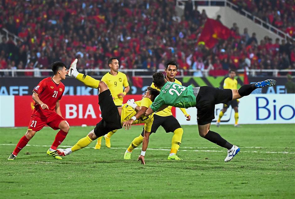 Caught in the middle: Malaysia’s Mohamad Zaquan Adha Abdul Radzak is challenged by Vietnam goalkeeper Dang Van Lam in the AFF Suzuki Cup second leg final at the MyDinh Stadium yesterday. Vietnam won 1-0 to emerge champions 3-2 on aggregate. Inset: Nguyen Anh Duc celebrating after scoring in the fifth minute. — Bernama