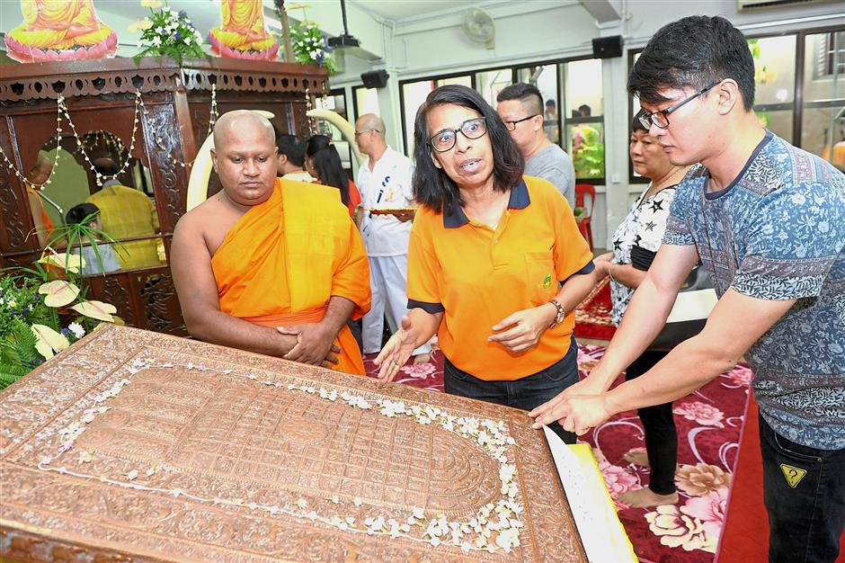 (Left pic) Dr Surya (centre) explaining about the enlarged Buddha footprint with 108 signs at the Wesak Day celebration at the Mahindarama Buddhist Temple in Jalan Kampar, Penang, while (right pic) devotees offer prayers at the temple’s main shrine.