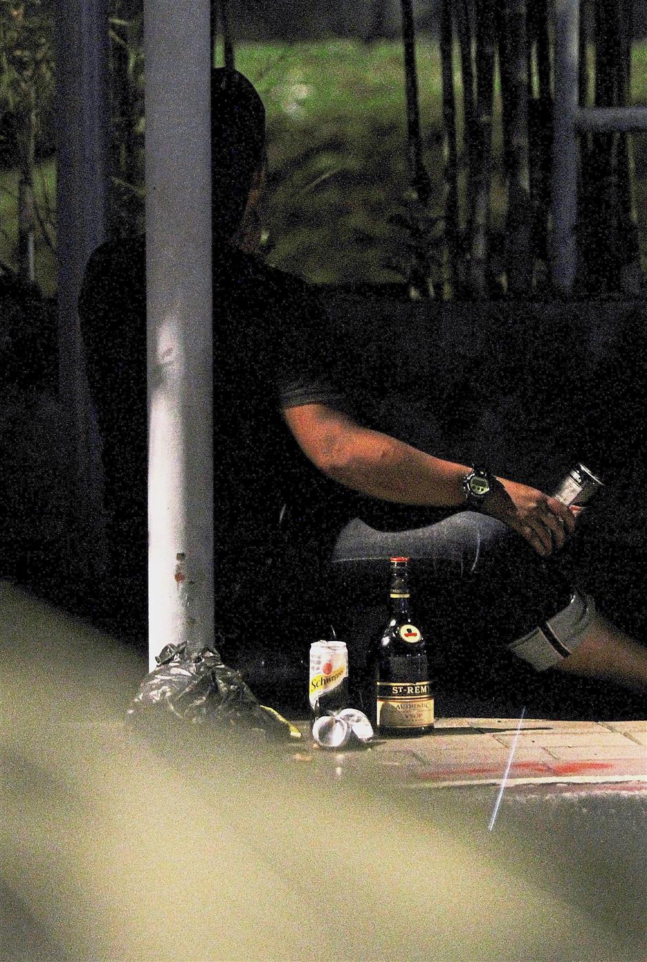 A man sitting in the shadows consuming liquor in Jalan Tebing Brickfields.