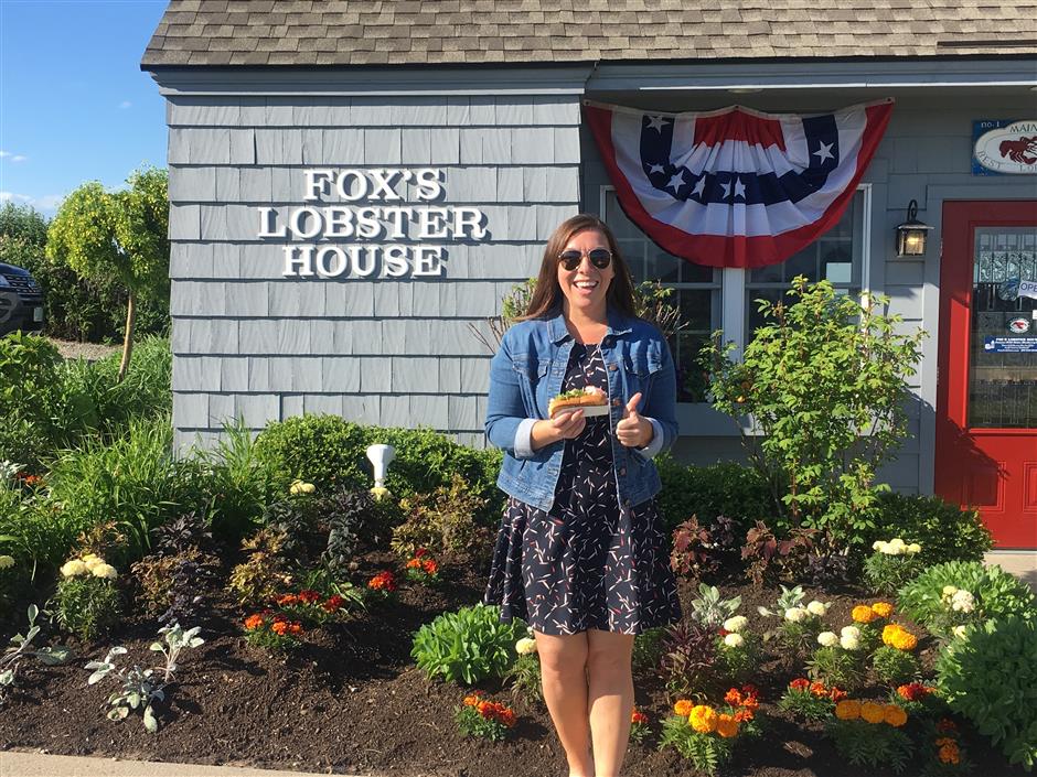 In this Friday, June 7, 2019, photo provided by Alicia Jessop, Jessop poses for a photo with a lobster roll at Fox's Lobster House in York, Maine. Jessop wanted to snap the perfect picture Friday of her lobster roll from Fox’s Lobster House in York, Maine, before she took a bite. She says she was focused on framing the sandwich with the picturesque Nubble Lighthouse in the background when she felt something rustle her hand. She quickly realized a seagull had knocked it out of her hand and was already eating it. (Alicia Jessop/@rulingsports via AP)