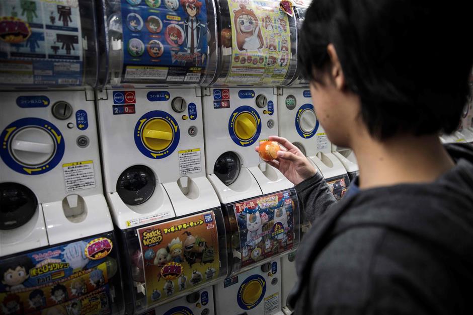 In this picture taken on November 14, 2017, a schoolboy on the hunt for capsule toys looks at his newly-dispensed item from a vending machine at a store in Tokyo's Akihabara district. Capsule toys have been around for more than 40 years but the craze really took off in 2012 when Tokyo-based manufacturer Kitan Club launched its 'Koppu no Fuchico' ('Fuchico at the edge of a glass'). The miniature trinkets nestled inside plastic bubbles have enjoyed huge success by targeting adults as well as children and riding the wave of social media as the ultimate 'Instagram-ready' accessory. / AFP PHOTO / Behrouz MEHRI / TO GO WITH AFP STORY JAPAN-TOYS-ENTERTAINMENT,FEATURE BY NATSUKO FUKUE