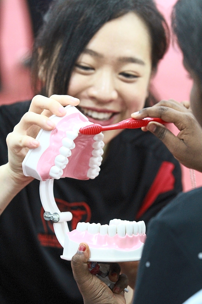 Volunteer Kayla Teh Khe Sin teaching a child from PPR Lembah Subang proper tooth-brushing techniques.