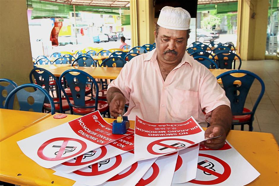In four languages: Restoran Alif Maju owner Abbas Abu Bakar preparing ‘no smoking’ signs for his outlet in Klang.
