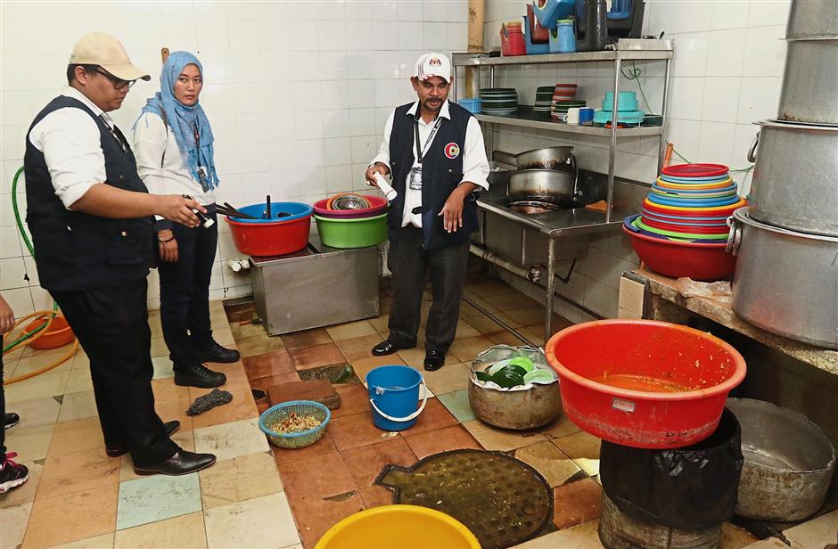 State Health enforcement officers looking at the washing area near a manhole cover at the back of one of the nasi kandar outlets.