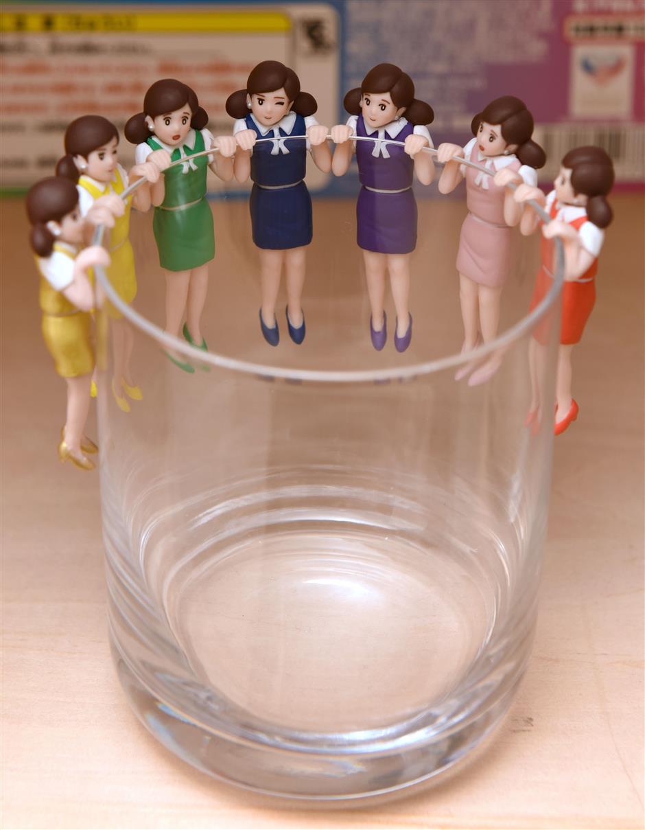 This photo taken on November 15, 2017 shows figurines of women wearing typical office clothes, whose arms are designed to hang over the edge of a glass, displayed at Tokyo-based manufacturer Kitan Club. Capsule toys have been around for more than 40 years but the craze really took off in 2012 when Tokyo-based manufacturer Kitan Club launched its 'Koppu no Fuchico' ('Fuchico at the edge of a glass'). The miniature trinkets nestled inside plastic bubbles have enjoyed huge success by targeting adults as well as children and riding the wave of social media as the ultimate 'Instagram-ready' accessory. / AFP PHOTO / Kazuhiro NOGI / TO GO WITH AFP STORY JAPAN-TOYS-ENTERTAINMENT,FEATURE BY NATSUKO FUKUE