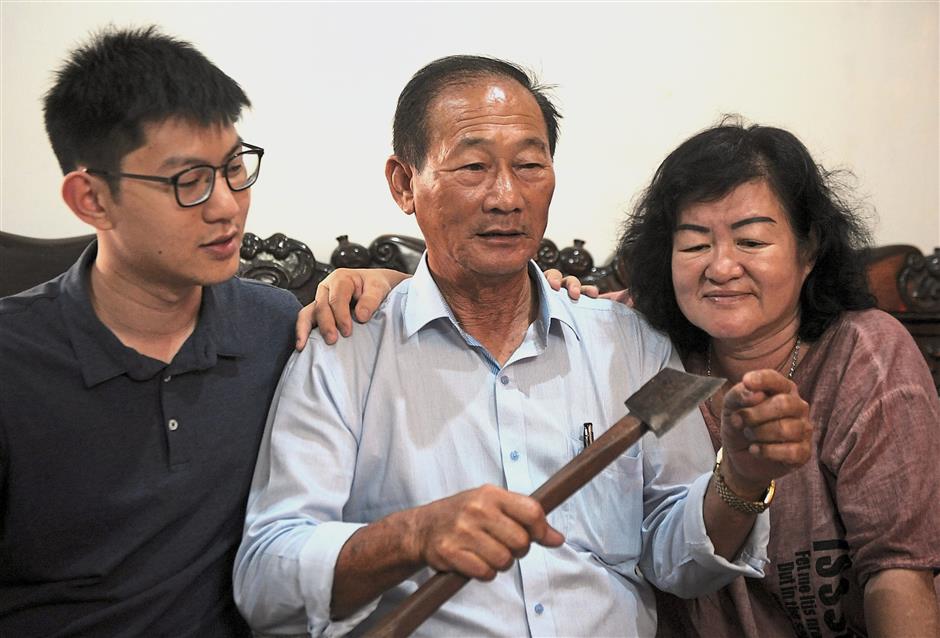 This is how I did it: Oon showing his wife, Tan Mooi Chen, 60, and son Chin Liang, 24, the axe he used to save the family. — ASRI ABDUL GHANI / The Star