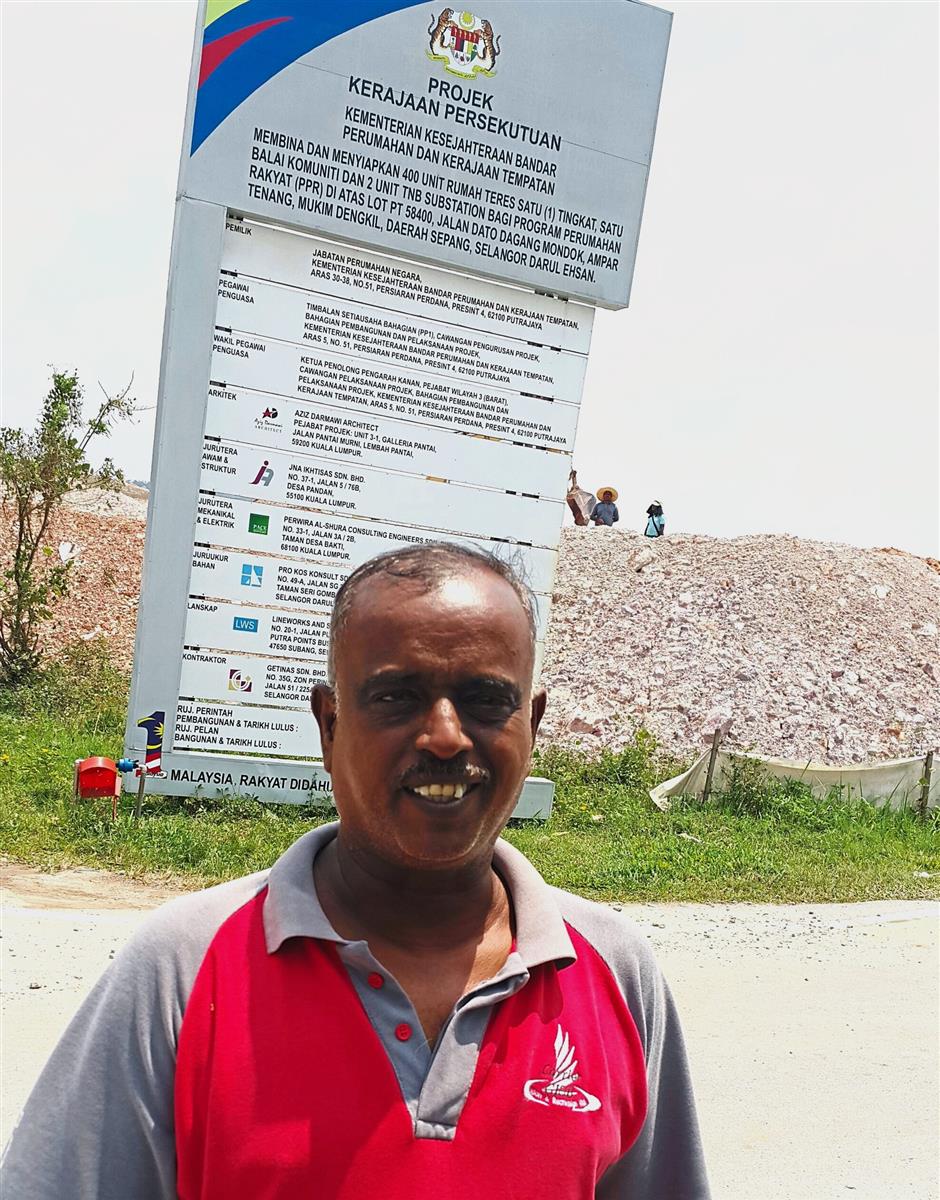 Ramadass is captured in a jubilant mood in front of a notice board at Ampar Tenang indicating that the housing project for the former estate workers is underway.